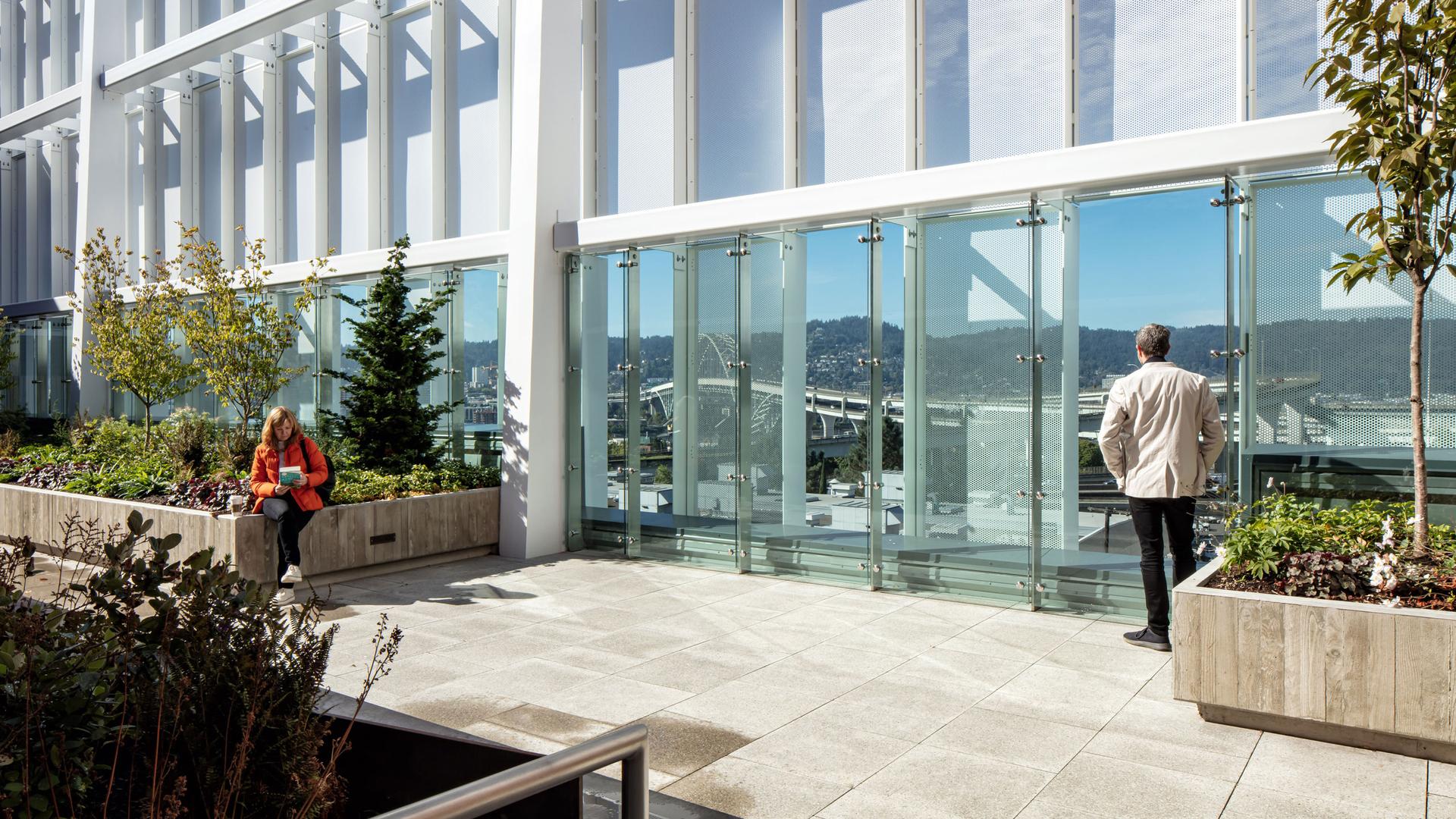 People in the therapeutic garden with planters and a reflection of the city on the building.
