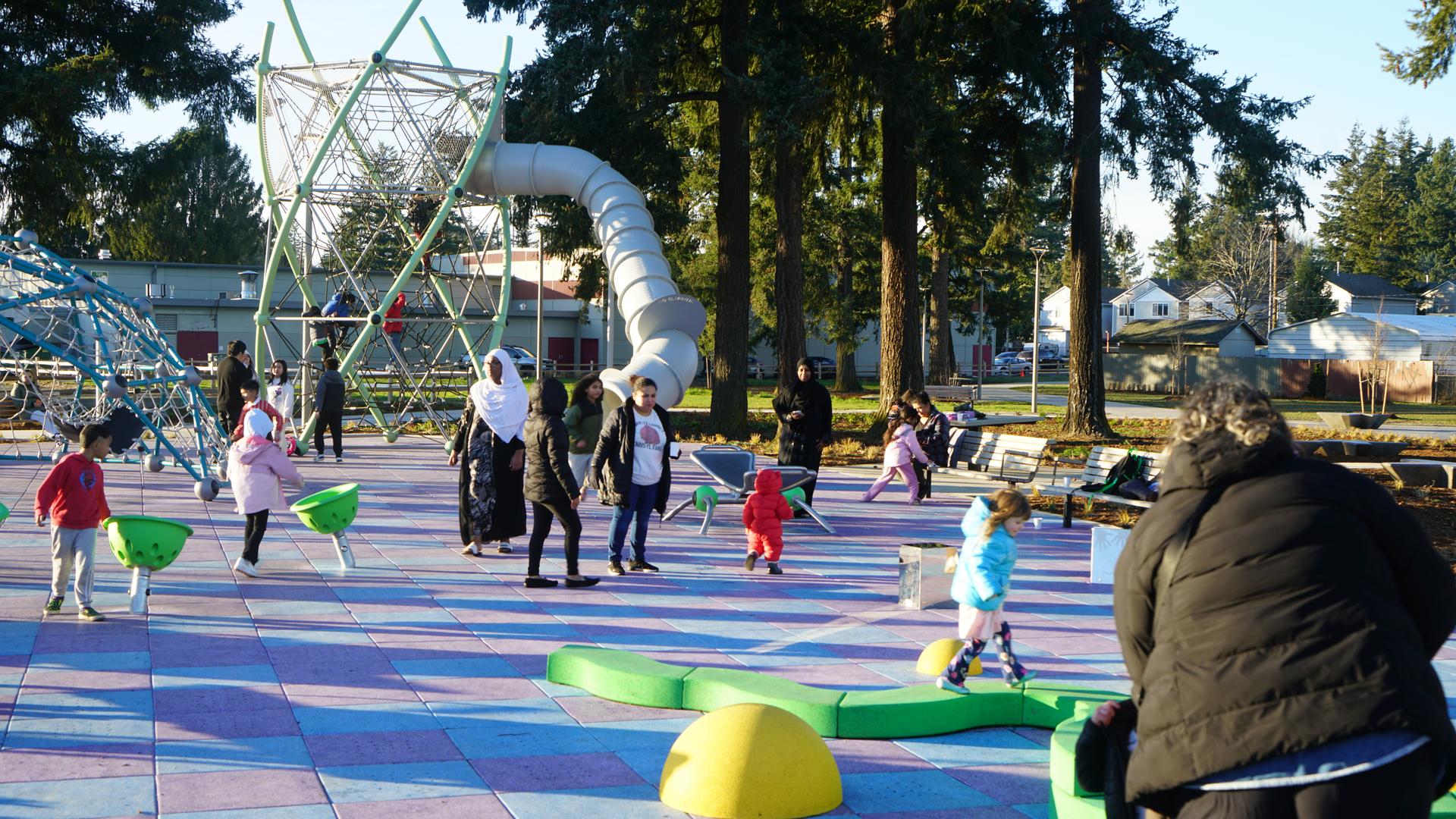 Children and families playing at the Mill Parks playground on a sunny day.