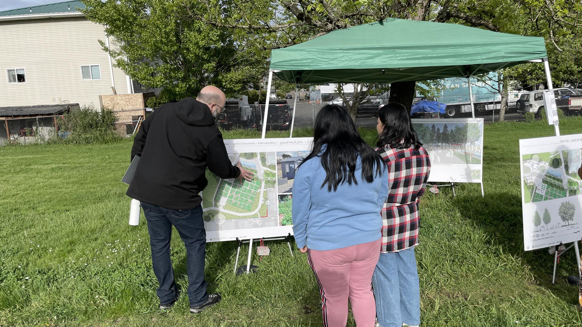 People reviewing park design boards under a canopy at an outdoor event.