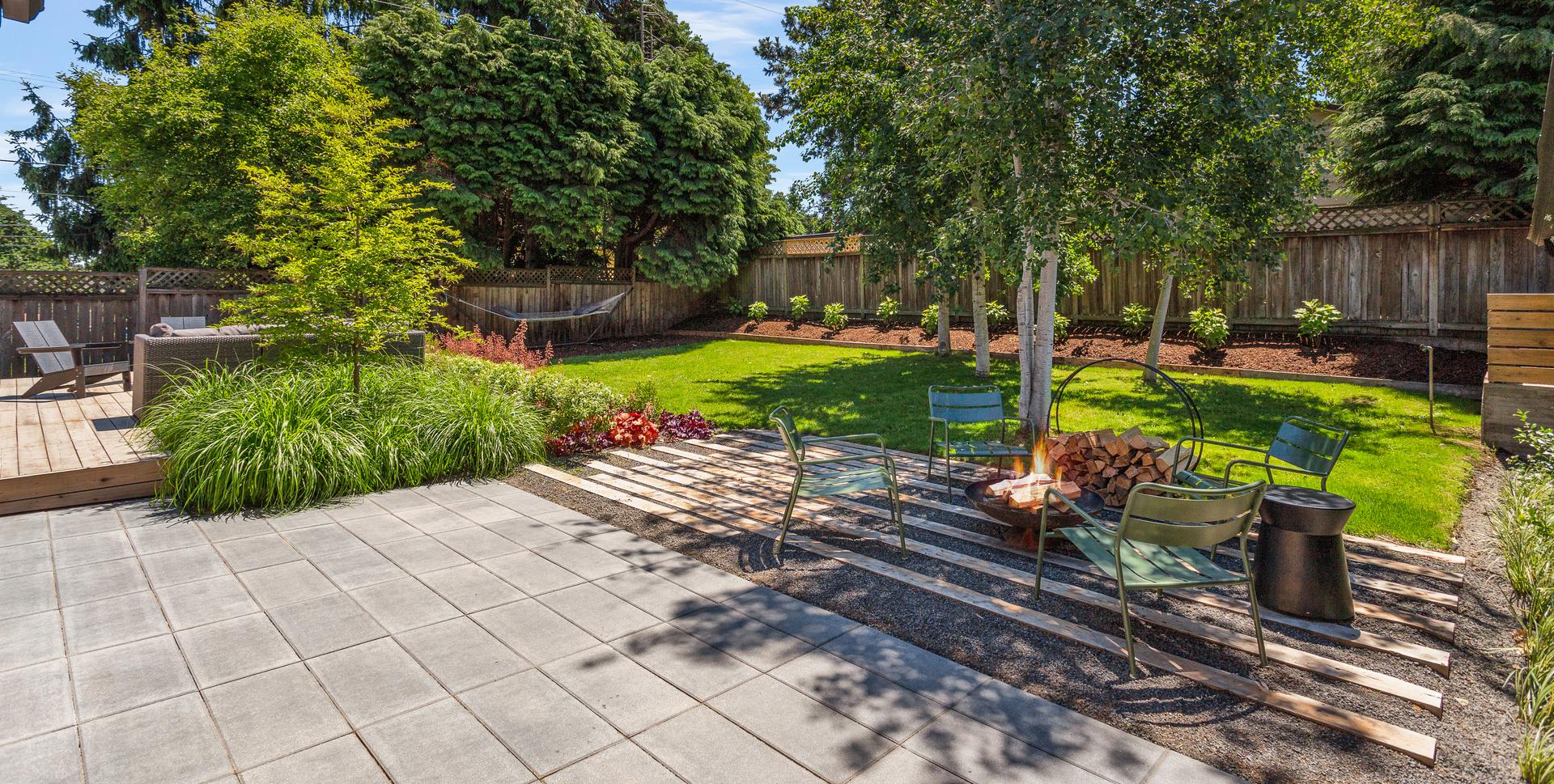 View of the back patio with a firepit, next to the deck, lawn, and aspen trees in a private residence in Portland.