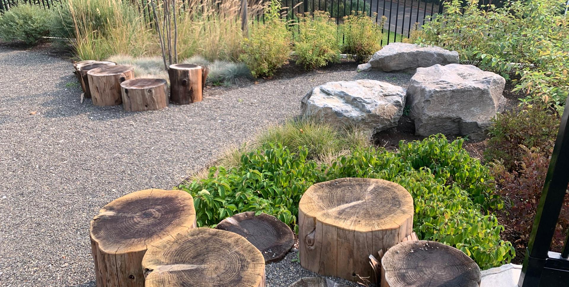 Nature play area with log and boulder seating surrounded by plantings at PCC Child Development Center.