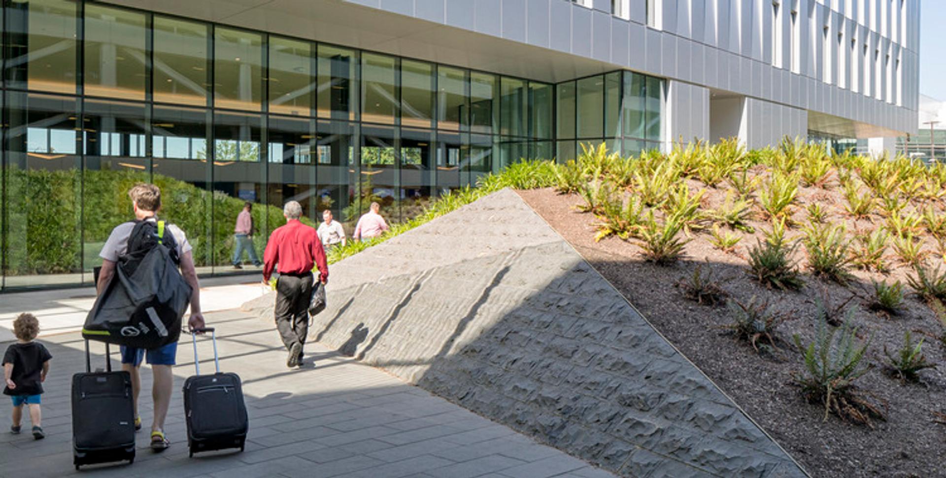 Travelers with luggage walking by landscaped mounds at the PACR entrance.